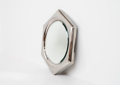 Space Age hexagon wall mirror (Italy, 1970s). A stunning piece made out of polished metal with a round inlay mirror and a beveled edge. It looks like one solid shiny piece and is a real eye catcher in the room. The mirror has several mounting points so that it can be hung in two different ways. In perfect condition.