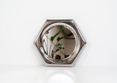 Space Age hexagon wall mirror (Italy, 1970s). A stunning piece made out of polished metal with a round inlay mirror and a beveled edge. It looks like one solid shiny piece and is a real eye catcher in the room. The mirror has several mounting points so that it can be hung in two different ways. In perfect condition.