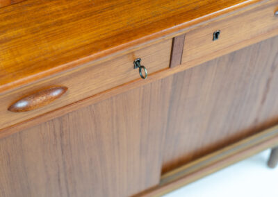 Teak secretary/bookcase by Harald Nielsen (Denmark, 1960s). A nicely designed and multifunctional piece containing four sliding doors, two drawers, a convenient pull-out leaf and some open storage space. Featuring nice handles and a warm natural wood grain. It is in splendid condition and the original key is included.
