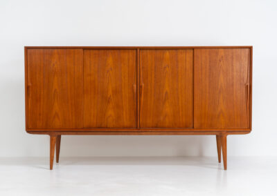 “Model 19” sideboard by Gunni Omann for Omann Jun (Denmark, 1960s). A high end teak piece containing four sliding doors, lots of storage space and eight convenient drawers on the inside. The combination of the typical Gunni Omann handles, the organic shapes and the warm golden woodgrain makes this a stunning Piece! The back is veneered aswell so it can be placed in the center of the room as a room divider for example. In very good condition, one of the handles has worn off a bit as shown on the pictures.