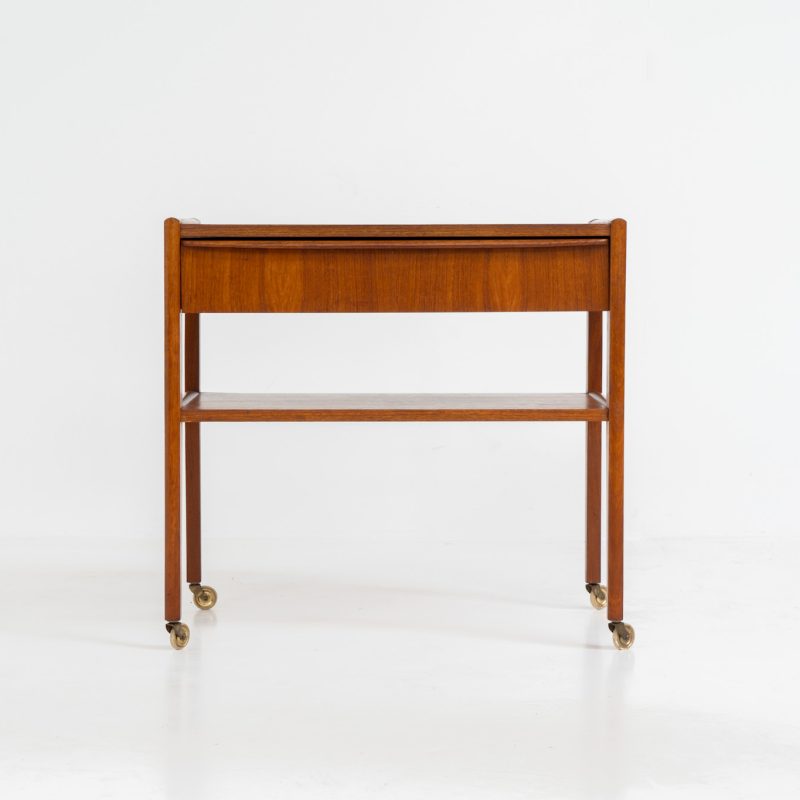 Danish trolley / sidetable in teak, 1960s A simple rolling sidetable with one drawer featuring a nicely sculpted handle, a warm woodgrain and some brass details on the wheels. In good condition with normal using traces.