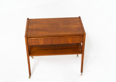Danish trolley / sidetable in teak, 1960s A simple rolling sidetable with one drawer featuring a nicely sculpted handle, a warm woodgrain and some brass details on the wheels. In good condition with normal using traces.