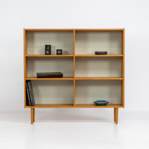 Oak bookcase by Domino Møbler (Denmark, 1960s). A simple bookcase in oak with a white back plate. It’s not very deep so it doesn’t take much space in the room. In good condition with some visible traces of wear and tear.