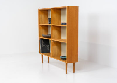 Oak bookcase by Domino Møbler (Denmark, 1960s). A simple bookcase in oak with a white back plate. It’s not very deep so it doesn’t take much space in the room. In good condition with some visible traces of wear and tear.