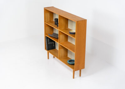 Oak bookcase by Domino Møbler (Denmark, 1960s). A simple bookcase in oak with a white back plate. It’s not very deep so it doesn’t take much space in the room. In good condition with some visible traces of wear and tear.