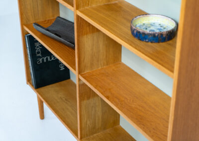 Oak bookcase by Domino Møbler (Denmark, 1960s). A simple bookcase in oak with a white back plate. It’s not very deep so it doesn’t take much space in the room. In good condition with some visible traces of wear and tear.