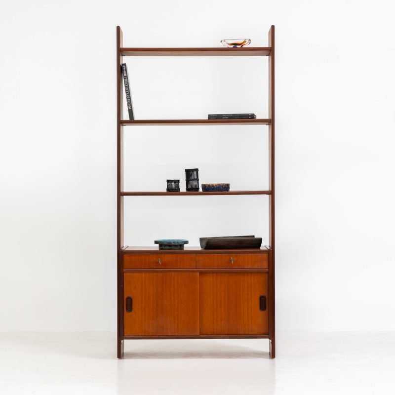 Teak shelving system / room devider (Sweden, 1960s). A very nice piece featuring two sliding doors, two drawers and three adjustable shelves. It’s sleek minimalist design combined with a wonderful warm woodgrain are a perfect match. With its finished back, this versatile piece can be used as a room divider aswell, making it a perfect addition to any space. In excellent condition! Comes with the original keys.