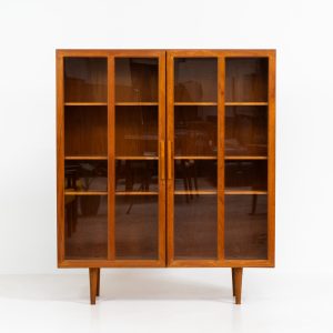 Teak showcase by Ib Kofod-Larsen for Faarup Møbelfabrik (Denmark, 1960s). This beautiful showcase features a stunning teak woodgrain with intricate details throughout. It has two doors with elegant handles and glass panels, providing a clear view of the interior. Inside, there are three adjustable shelves, offering lots of storage options. It is in perfect condition and labeled by maker.