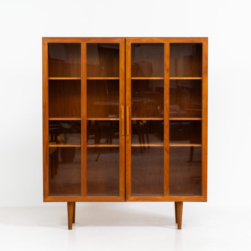 Teak showcase by Ib Kofod-Larsen for Faarup Møbelfabrik (Denmark, 1960s). This beautiful showcase features a stunning teak woodgrain with intricate details throughout. It has two doors with elegant handles and glass panels, providing a clear view of the interior. Inside, there are three adjustable shelves, offering lots of storage options. It is in perfect condition and labeled by maker.