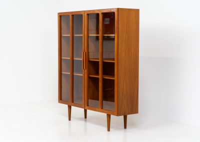 Teak showcase by Ib Kofod-Larsen for Faarup Møbelfabrik (Denmark, 1960s). This beautiful showcase features a stunning teak woodgrain with intricate details throughout. It has two doors with elegant handles and glass panels, providing a clear view of the interior. Inside, there are three adjustable shelves, offering lots of storage options. It is in perfect condition and labeled by maker.