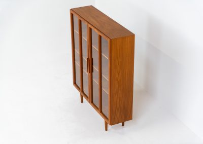 Teak showcase by Ib Kofod-Larsen for Faarup Møbelfabrik (Denmark, 1960s). This beautiful showcase features a stunning teak woodgrain with intricate details throughout. It has two doors with elegant handles and glass panels, providing a clear view of the interior. Inside, there are three adjustable shelves, offering lots of storage options. It is in perfect condition and labeled by maker.