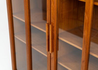 Teak showcase by Ib Kofod-Larsen for Faarup Møbelfabrik (Denmark, 1960s). This beautiful showcase features a stunning teak woodgrain with intricate details throughout. It has two doors with elegant handles and glass panels, providing a clear view of the interior. Inside, there are three adjustable shelves, offering lots of storage options. It is in perfect condition and labeled by maker.
