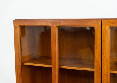 Teak showcase by Ib Kofod-Larsen for Faarup Møbelfabrik (Denmark, 1960s). This beautiful showcase features a stunning teak woodgrain with intricate details throughout. It has two doors with elegant handles and glass panels, providing a clear view of the interior. Inside, there are three adjustable shelves, offering lots of storage options. It is in perfect condition and labeled by maker.