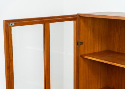 Teak showcase by Ib Kofod-Larsen for Faarup Møbelfabrik (Denmark, 1960s). This beautiful showcase features a stunning teak woodgrain with intricate details throughout. It has two doors with elegant handles and glass panels, providing a clear view of the interior. Inside, there are three adjustable shelves, offering lots of storage options. It is in perfect condition and labeled by maker.