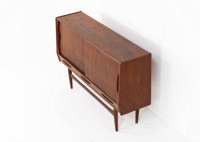 Teak highboard by Jensen & Mølholm (Denmark, 1960s). This stunning piece features two large sliding doors, three drawers, and lots of internal storage with three adjustable shelves and two small drawers. Crafted from warm, natural-looking teak, it showcases beautiful organic curves and elegant bent plywood handles. It is in very good condition with mild age marks and a little color difference on the left panel, as shown on the picture