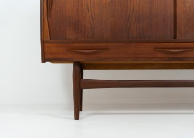 Teak highboard by Jensen & Mølholm (Denmark, 1960s). This stunning piece features two large sliding doors, three drawers, and lots of internal storage with three adjustable shelves and two small drawers. Crafted from warm, natural-looking teak, it showcases beautiful organic curves and elegant bent plywood handles. It is in very good condition with mild age marks and a little color difference on the left panel, as shown on the picture