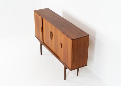 Danish highboard in teak, 1960s. A beautiful mid-century piece crafted in rich teak wood, featuring two spacious doors and two smooth-sliding doors, offering lots of storage and a stylish bar unit inside. The highboard showcases a warm, natural woodgrain, elegant rounded edges, and distinctive handles. It is in very good condition with mild age-related marks.