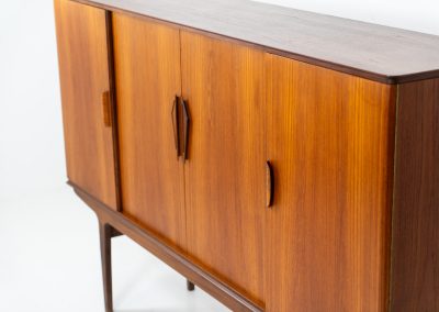 Danish highboard in teak, 1960s. A beautiful mid-century piece crafted in rich teak wood, featuring two spacious doors and two smooth-sliding doors, offering lots of storage and a stylish bar unit inside. The highboard showcases a warm, natural woodgrain, elegant rounded edges, and distinctive handles. It is in very good condition with mild age-related marks.