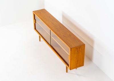 Stunning sideboard with glass doors by CFC Silkeborg (Denmark, 1960s). This elegant mid-century piece, crafted in teak, features beautifully rounded edges, sleek glass sliding doors, and refined wooden handles. Its timeless design combines style with functionality, offering lots of storage space with two adjustable shelves inside. Notably versatile, the sideboard includes three wall mounts on the back, allowing it to be used as a floating sideboard if desired. The legs can be easily removed for this purpose. In very good condition, with only two small repair marks.