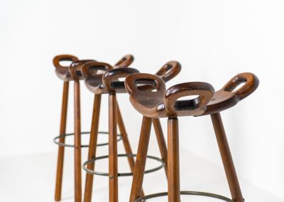 Set of 3 Brutalist “Marbella” stools manufactured by Conoform and attributed to Sergio Rodrigues (Spain, 1970s). This iconic set of Marbella stools, also known as the “Spanish Stool,” exemplifies brutalist design with a sculptural flair. Crafted from solid beech wood, the stools feature a distinctive curved seat and are complemented by a sturdy iron footrest. The set is in good vintage condition, displaying some signs of use such as seat marks and wear consistent with age.