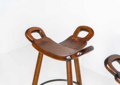 Set of 3 Brutalist “Marbella” stools manufactured by Conoform and attributed to Sergio Rodrigues (Spain, 1970s). This iconic set of Marbella stools, also known as the “Spanish Stool,” exemplifies brutalist design with a sculptural flair. Crafted from solid beech wood, the stools feature a distinctive curved seat and are complemented by a sturdy iron footrest. The set is in good vintage condition, displaying some signs of use such as seat marks and wear consistent with age.