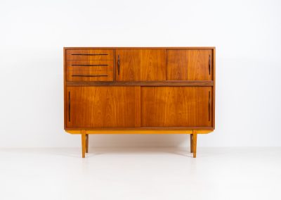 Danish highboard in teak, 1960s. A beautiful mid-century piece crafted in rich teak and standing on oak base, featuring lots of storage space and contrasting black handels. The highboard showcases a warm, natural woodgrain, sleek lines, and distinctive handles. It is in excellent condition with some minor using traces on the top.