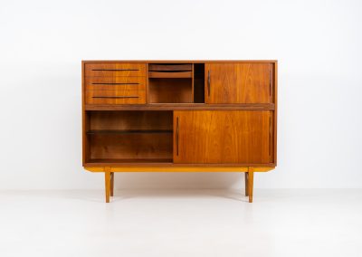Danish highboard in teak, 1960s. A beautiful mid-century piece crafted in rich teak and standing on oak base, featuring lots of storage space and contrasting black handels. The highboard showcases a warm, natural woodgrain, sleek lines, and distinctive handles. It is in excellent condition with some minor using traces on the top.