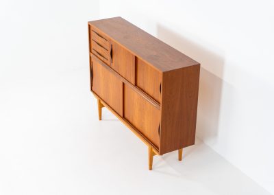 Danish highboard in teak, 1960s. A beautiful mid-century piece crafted in rich teak and standing on oak base, featuring lots of storage space and contrasting black handels. The highboard showcases a warm, natural woodgrain, sleek lines, and distinctive handles. It is in excellent condition with some minor using traces on the top.