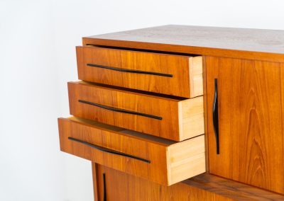 Danish highboard in teak, 1960s. A beautiful mid-century piece crafted in rich teak and standing on oak base, featuring lots of storage space and contrasting black handels. The highboard showcases a warm, natural woodgrain, sleek lines, and distinctive handles. It is in excellent condition with some minor using traces on the top.