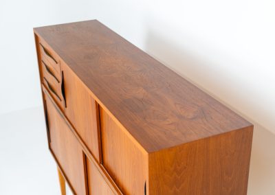 Danish highboard in teak, 1960s. A beautiful mid-century piece crafted in rich teak and standing on oak base, featuring lots of storage space and contrasting black handels. The highboard showcases a warm, natural woodgrain, sleek lines, and distinctive handles. It is in excellent condition with some minor using traces on the top.