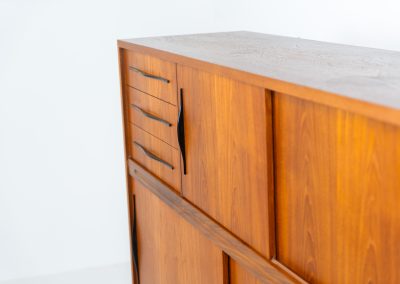 Danish highboard in teak, 1960s. A beautiful mid-century piece crafted in rich teak and standing on oak base, featuring lots of storage space and contrasting black handels. The highboard showcases a warm, natural woodgrain, sleek lines, and distinctive handles. It is in excellent condition with some minor using traces on the top.