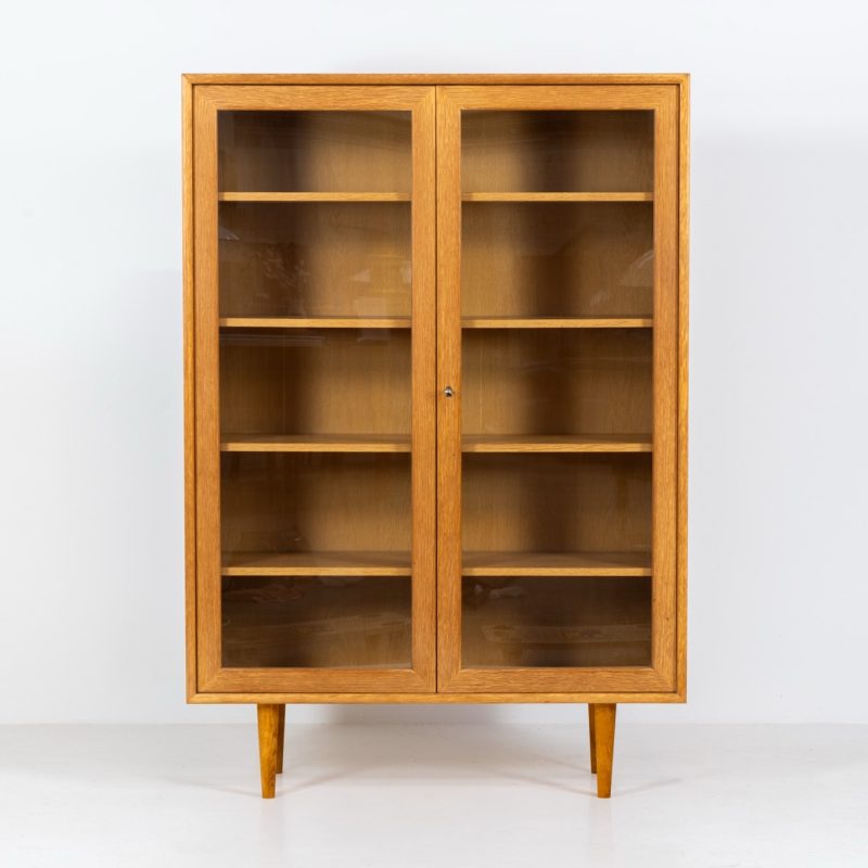 Oak showcase by WK Möbel (Germany, 1970s). This beautiful showcase features a stunning aged oak woodgrain and has two handle-less doors with glass panels, providing a clear view of the interior. Inside, there are four adjustable shelves, offering lots of storage options. It is in very good condition and labeled by maker.