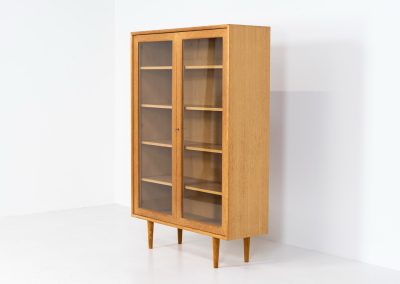 Oak showcase by WK Möbel (Germany, 1970s). This beautiful showcase features a stunning aged oak woodgrain and has two handle-less doors with glass panels, providing a clear view of the interior. Inside, there are four adjustable shelves, offering lots of storage options. It is in very good condition and labeled by maker.