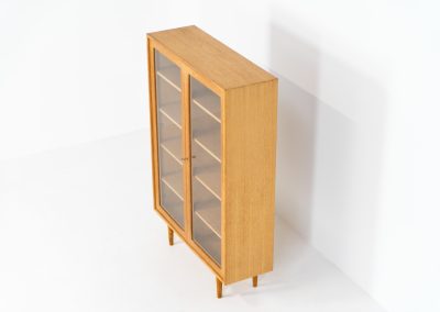 Oak showcase by WK Möbel (Germany, 1970s). This beautiful showcase features a stunning aged oak woodgrain and has two handle-less doors with glass panels, providing a clear view of the interior. Inside, there are four adjustable shelves, offering lots of storage options. It is in very good condition and labeled by maker.