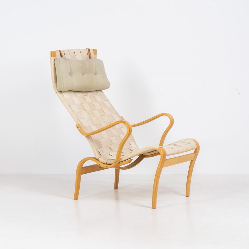 “Miranda” easy chair by Bruno Mathsson Design Studio (Sweden, 1970s). Originally designed by Bruno Mathsson in 1941, this exceptional “Miranda” easy chair was manufactured in the 1970s. It features a beautifully curved, molded beech plywood frame with a linen webbing seat and an adjustable headrest, suspended by leather straps. The chair is in good vintage condition, showing signs of use such as marks, fabric fraying, and some damage to the wood, all of which add to its authentic character. Marked by maker.