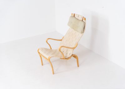 “Miranda” easy chair by Bruno Mathsson Design Studio (Sweden, 1970s). Originally designed by Bruno Mathsson in 1941, this exceptional “Miranda” easy chair was manufactured in the 1970s. It features a beautifully curved, molded beech plywood frame with a linen webbing seat and an adjustable headrest, suspended by leather straps. The chair is in good vintage condition, showing signs of use such as marks, fabric fraying, and some damage to the wood, all of which add to its authentic character. Marked by maker.