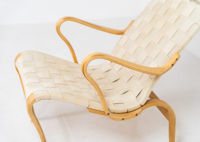 “Miranda” easy chair by Bruno Mathsson Design Studio (Sweden, 1970s). Originally designed by Bruno Mathsson in 1941, this exceptional “Miranda” easy chair was manufactured in the 1970s. It features a beautifully curved, molded beech plywood frame with a linen webbing seat and an adjustable headrest, suspended by leather straps. The chair is in good vintage condition, showing signs of use such as marks, fabric fraying, and some damage to the wood, all of which add to its authentic character. Marked by maker.