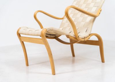 “Miranda” easy chair by Bruno Mathsson Design Studio (Sweden, 1970s). Originally designed by Bruno Mathsson in 1941, this exceptional “Miranda” easy chair was manufactured in the 1970s. It features a beautifully curved, molded beech plywood frame with a linen webbing seat and an adjustable headrest, suspended by leather straps. The chair is in good vintage condition, showing signs of use such as marks, fabric fraying, and some damage to the wood, all of which add to its authentic character. Marked by maker.