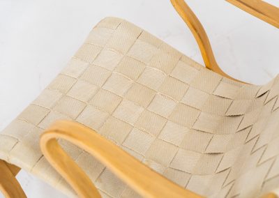 “Miranda” easy chair by Bruno Mathsson Design Studio (Sweden, 1970s). Originally designed by Bruno Mathsson in 1941, this exceptional “Miranda” easy chair was manufactured in the 1970s. It features a beautifully curved, molded beech plywood frame with a linen webbing seat and an adjustable headrest, suspended by leather straps. The chair is in good vintage condition, showing signs of use such as marks, fabric fraying, and some damage to the wood, all of which add to its authentic character. Marked by maker.