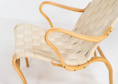 “Miranda” easy chair by Bruno Mathsson Design Studio (Sweden, 1970s). Originally designed by Bruno Mathsson in 1941, this exceptional “Miranda” easy chair was manufactured in the 1970s. It features a beautifully curved, molded beech plywood frame with a linen webbing seat and an adjustable headrest, suspended by leather straps. The chair is in good vintage condition, showing signs of use such as marks, fabric fraying, and some damage to the wood, all of which add to its authentic character. Marked by maker.