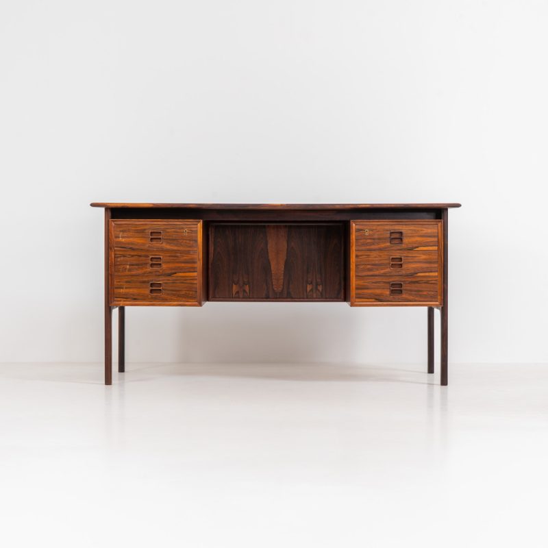 Exceptional writing desk in rosewood by Edmund Brouer for Brouer Møbelfabrik (Denmark, 1960s). This stunning freestanding desk is a true statement piece. Crafted from rosewood, it features a generous work surface, six spacious drawers, and the most beautiful woodgrain. The back of the desk features three open bookshelves, adding both functionality and aesthetic appeal. Often mistakenly attributed to Arne Vodder for Sibast, this iconic design is in fact the work of Edmund Brouer. The desk is in very good condition with some small discoloration due to water on the left shelves, as shown on the pictures.