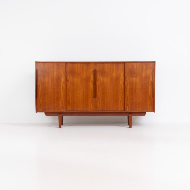 Danish highboard in teak, 1960s. A beautiful mid-century piece crafted in rich teak wood, featuring four spacious sliding doors and offering lots of storage with five drawers and two large shelves on the inside. The highboard showcases a warm, natural woodgrain, a sleek appearance, and distinctive sculpted handles and legs. It is in very good condition!