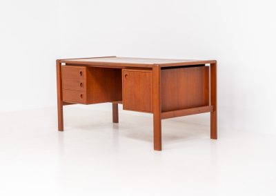Rare executive writing desk by H.P. Hansen (Denmark, 1950s). This large and exceptionally beautiful piece is a true example of top-quality Danish craftsmanship. Made from solid teak, it showcases elegant aesthetics with softly rounded edges and sculptural inset handles. The spacious desktop highlights a striking wood grain and is complemented by three drawers, a cabinet, and two open shelves at the back. The desk is finished on both sides, making it an ideal statement piece for placement in the center of a room. It is in excellent condition, with only minor discoloration on the top and light signs of use on the drawers.