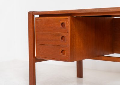 Rare executive writing desk by H.P. Hansen (Denmark, 1950s). This large and exceptionally beautiful piece is a true example of top-quality Danish craftsmanship. Made from solid teak, it showcases elegant aesthetics with softly rounded edges and sculptural inset handles. The spacious desktop highlights a striking wood grain and is complemented by three drawers, a cabinet, and two open shelves at the back. The desk is finished on both sides, making it an ideal statement piece for placement in the center of a room. It is in excellent condition, with only minor discoloration on the top and light signs of use on the drawers.