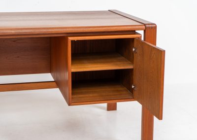 Rare executive writing desk by H.P. Hansen (Denmark, 1950s). This large and exceptionally beautiful piece is a true example of top-quality Danish craftsmanship. Made from solid teak, it showcases elegant aesthetics with softly rounded edges and sculptural inset handles. The spacious desktop highlights a striking wood grain and is complemented by three drawers, a cabinet, and two open shelves at the back. The desk is finished on both sides, making it an ideal statement piece for placement in the center of a room. It is in excellent condition, with only minor discoloration on the top and light signs of use on the drawers.