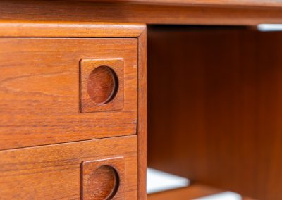 Rare executive writing desk by H.P. Hansen (Denmark, 1950s). This large and exceptionally beautiful piece is a true example of top-quality Danish craftsmanship. Made from solid teak, it showcases elegant aesthetics with softly rounded edges and sculptural inset handles. The spacious desktop highlights a striking wood grain and is complemented by three drawers, a cabinet, and two open shelves at the back. The desk is finished on both sides, making it an ideal statement piece for placement in the center of a room. It is in excellent condition, with only minor discoloration on the top and light signs of use on the drawers.