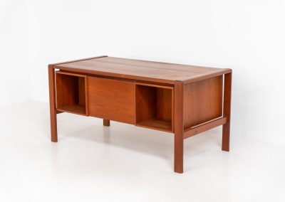 Rare executive writing desk by H.P. Hansen (Denmark, 1950s). This large and exceptionally beautiful piece is a true example of top-quality Danish craftsmanship. Made from solid teak, it showcases elegant aesthetics with softly rounded edges and sculptural inset handles. The spacious desktop highlights a striking wood grain and is complemented by three drawers, a cabinet, and two open shelves at the back. The desk is finished on both sides, making it an ideal statement piece for placement in the center of a room. It is in excellent condition, with only minor discoloration on the top and light signs of use on the drawers.