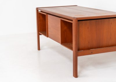 Rare executive writing desk by H.P. Hansen (Denmark, 1950s). This large and exceptionally beautiful piece is a true example of top-quality Danish craftsmanship. Made from solid teak, it showcases elegant aesthetics with softly rounded edges and sculptural inset handles. The spacious desktop highlights a striking wood grain and is complemented by three drawers, a cabinet, and two open shelves at the back. The desk is finished on both sides, making it an ideal statement piece for placement in the center of a room. It is in excellent condition, with only minor discoloration on the top and light signs of use on the drawers.