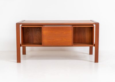 Rare executive writing desk by H.P. Hansen (Denmark, 1950s). This large and exceptionally beautiful piece is a true example of top-quality Danish craftsmanship. Made from solid teak, it showcases elegant aesthetics with softly rounded edges and sculptural inset handles. The spacious desktop highlights a striking wood grain and is complemented by three drawers, a cabinet, and two open shelves at the back. The desk is finished on both sides, making it an ideal statement piece for placement in the center of a room. It is in excellent condition, with only minor discoloration on the top and light signs of use on the drawers.
