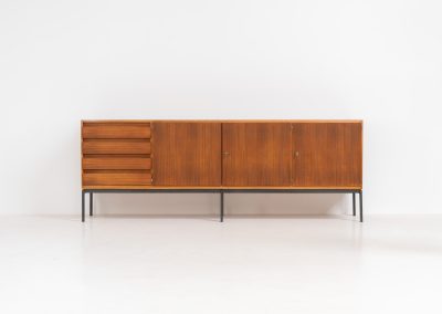 XL Modernist sideboard by Behr Möbel (Germany, 1950s). This striking modernist sideboard was produced in the 1950s by the renowned German manufacturer Behr Möbel, best known for the iconic B40 model. Expertly crafted from rich teak wood, the piece rests on a sleek metal base that adds to its architectural presence. It features four drawers and three doors, offering generous storage space with adjustable shelves inside. The sideboard is in very good condition, with fully functional locks.